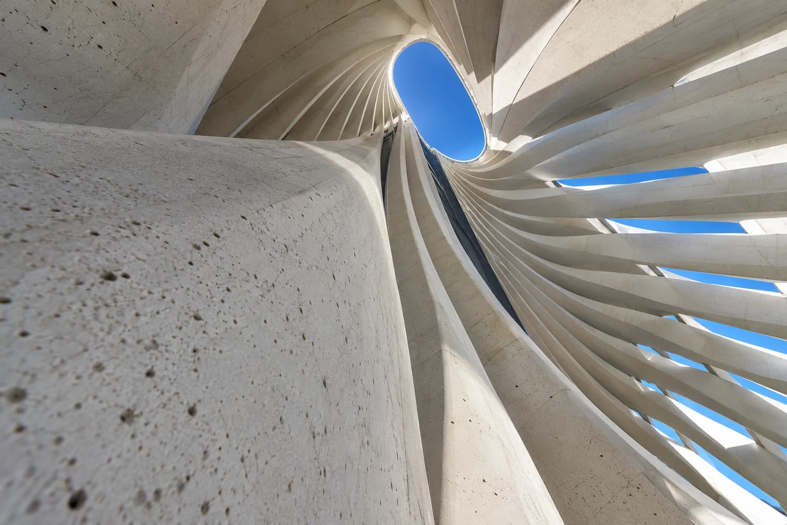 A dramatic upward view of white contemporary architectural ribs against a deep blue sky